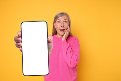 Mature woman showing mobile phone with blank screen on golden background. Mockup for design
