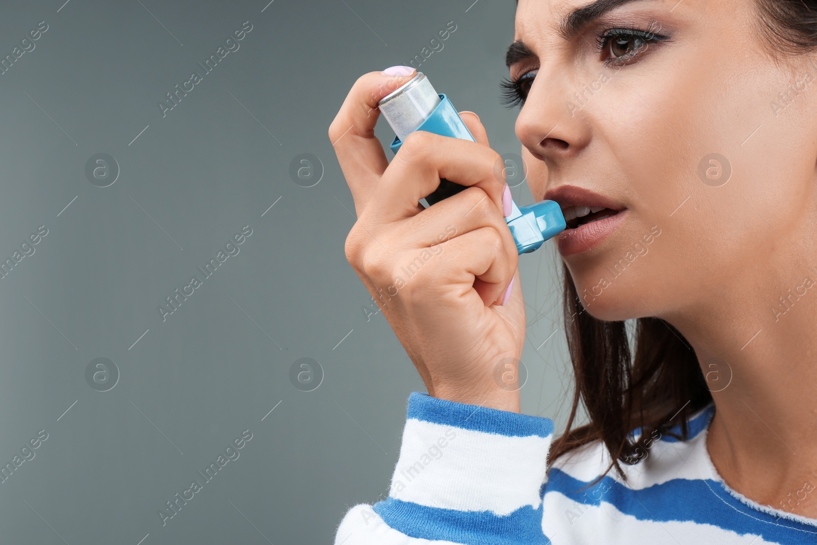 Photo of Young woman using asthma inhaler on color background, closeup