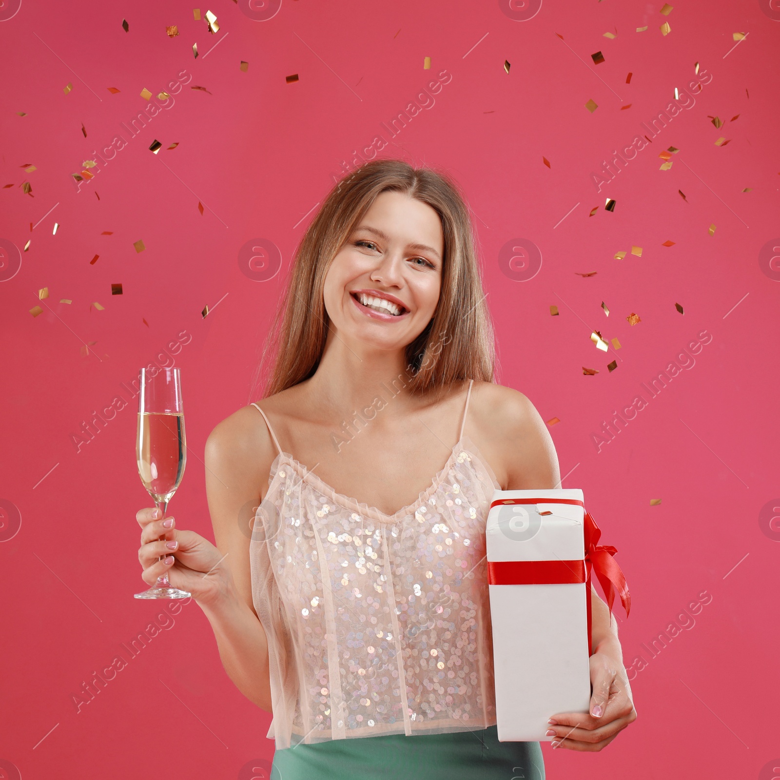 Photo of Happy young woman with Christmas gift and glass of champagne on pink background