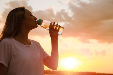 Photo of Young woman drinking water to prevent heat stroke outdoors at sunset, space for text