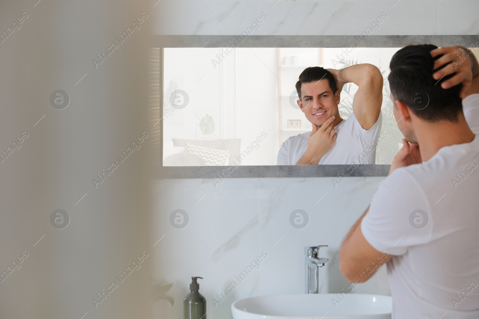 Photo of Handsome man touching his smooth face after shaving near mirror in bathroom