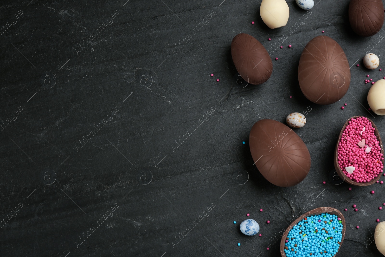 Photo of Sweet chocolate eggs and sprinkles on black table, flat lay. Space for text