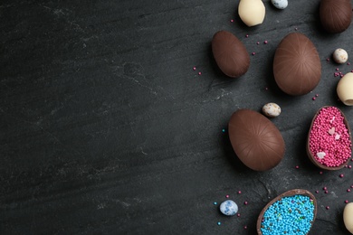 Sweet chocolate eggs and sprinkles on black table, flat lay. Space for text