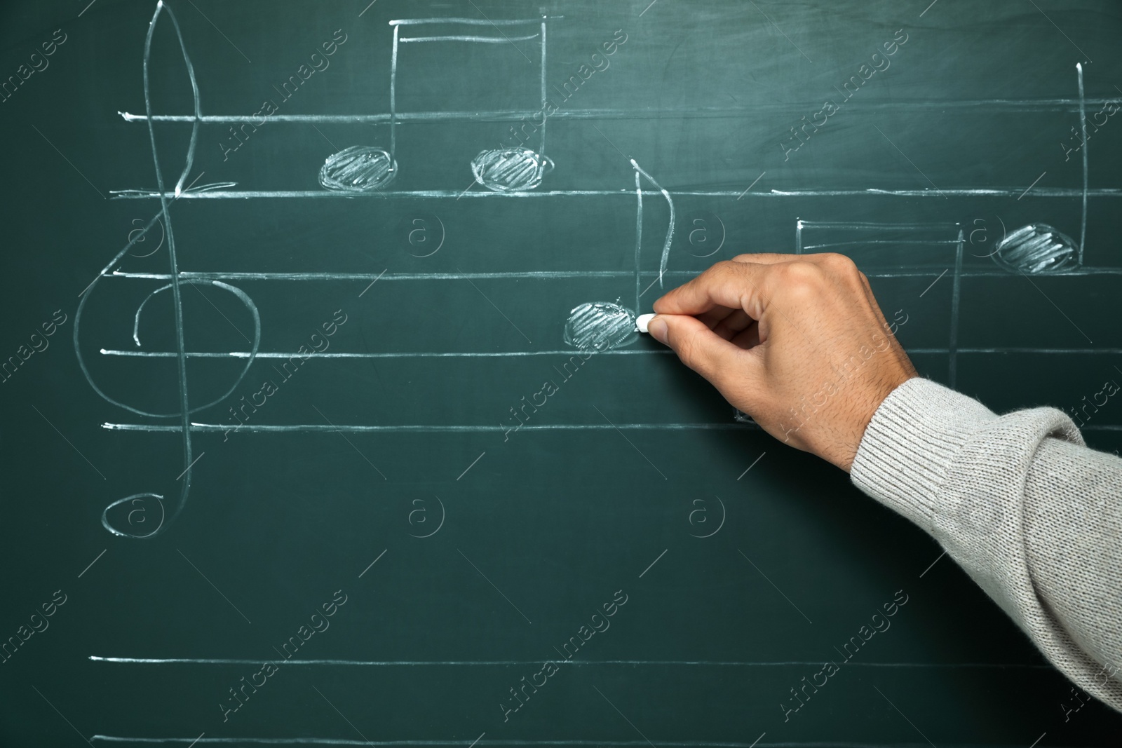 Photo of Teacher writing music notes with chalk on greenboard, closeup