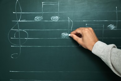 Photo of Teacher writing music notes with chalk on greenboard, closeup