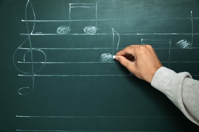 Teacher writing music notes with chalk on greenboard, closeup