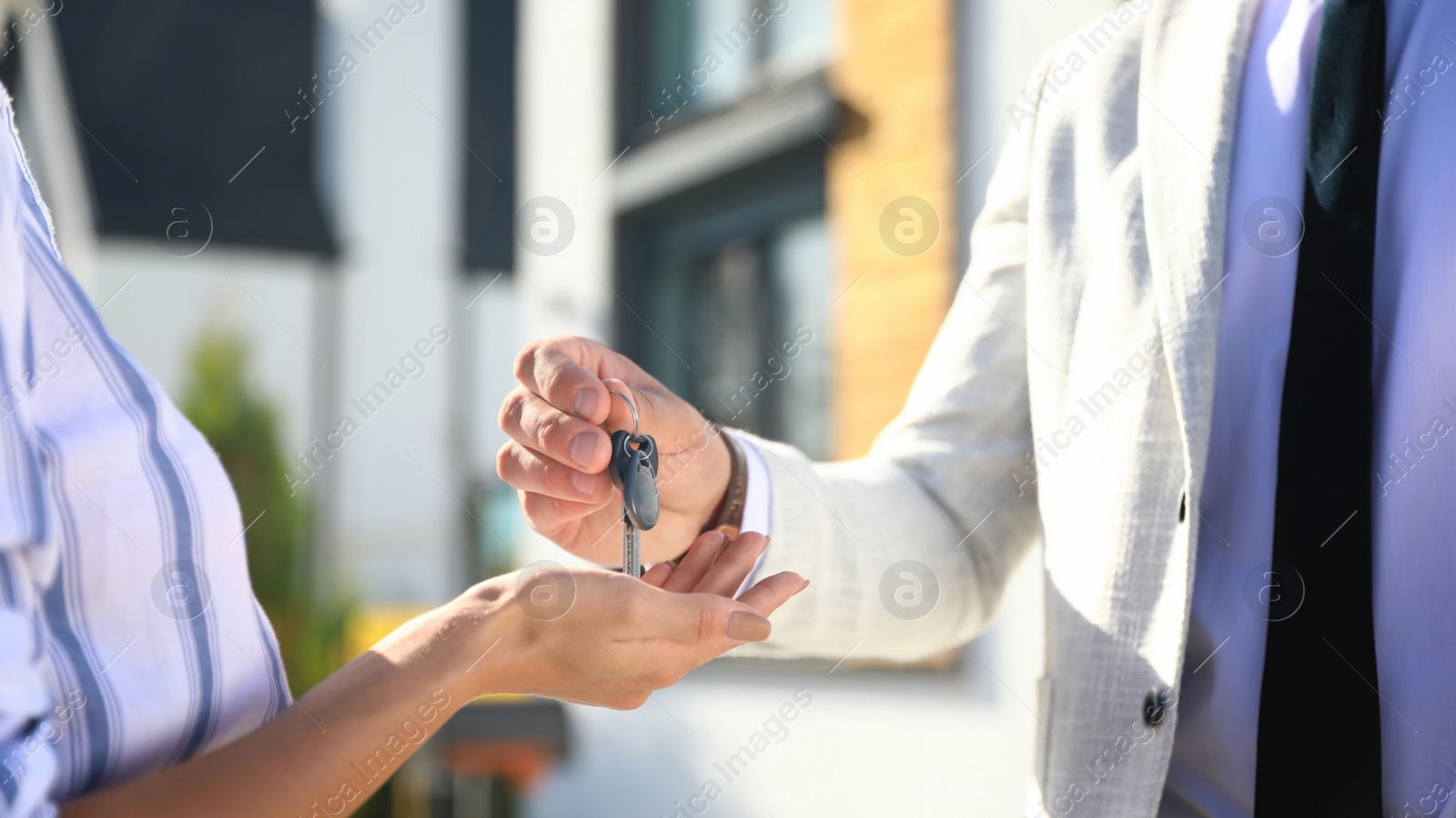 Photo of Real estate agent giving house keys to young woman outdoors, closeup