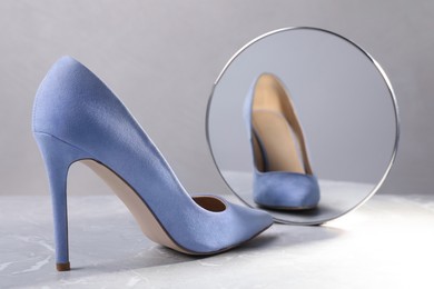 Photo of Stylish high heeled shoe in front of mirror on grey table. Vanity concept