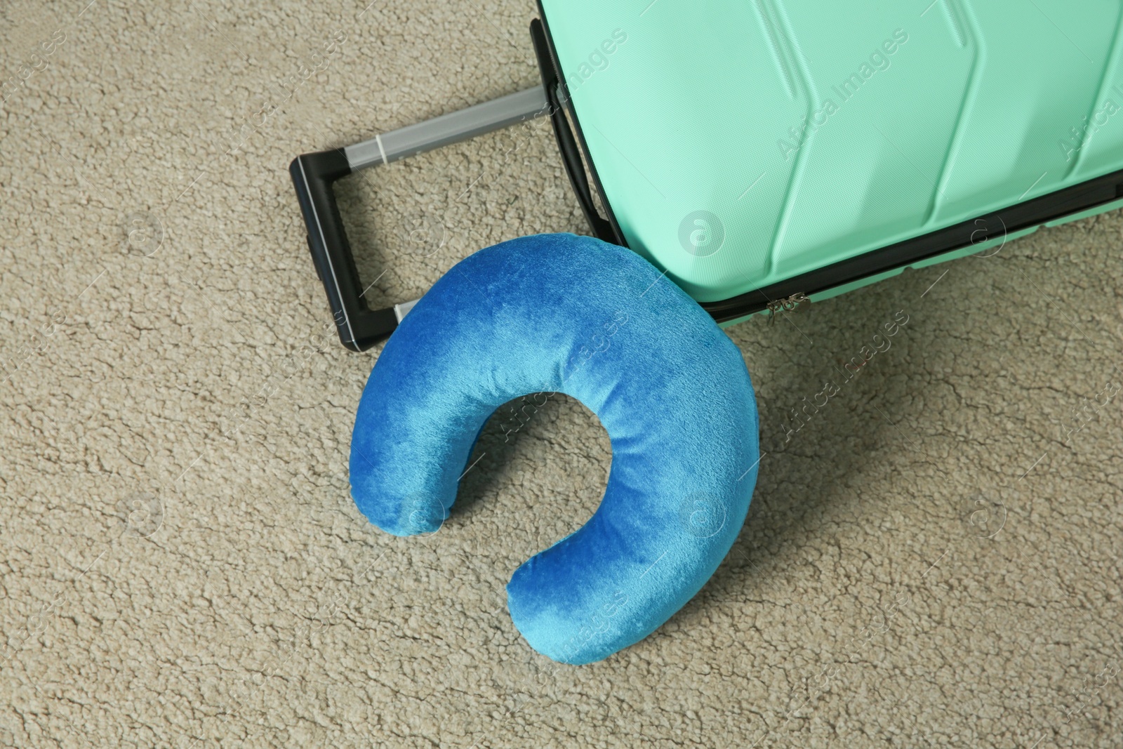 Photo of Light blue travel pillow and suitcase on beige rug, flat lay