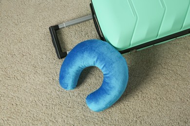 Photo of Light blue travel pillow and suitcase on beige rug, flat lay