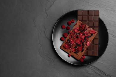 Photo of Plate and different chocolate bars with freeze dried fruits on slate table, top view. Space for text