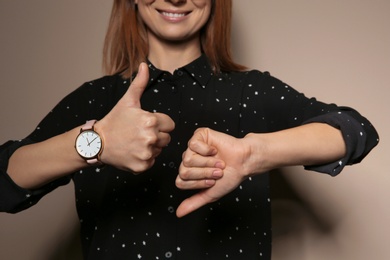 Woman showing THUMB UP and DOWN gesture in sign language on color background, closeup