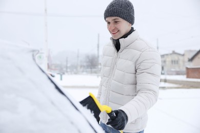 Photo of Man cleaning snow from car with brush outdoors