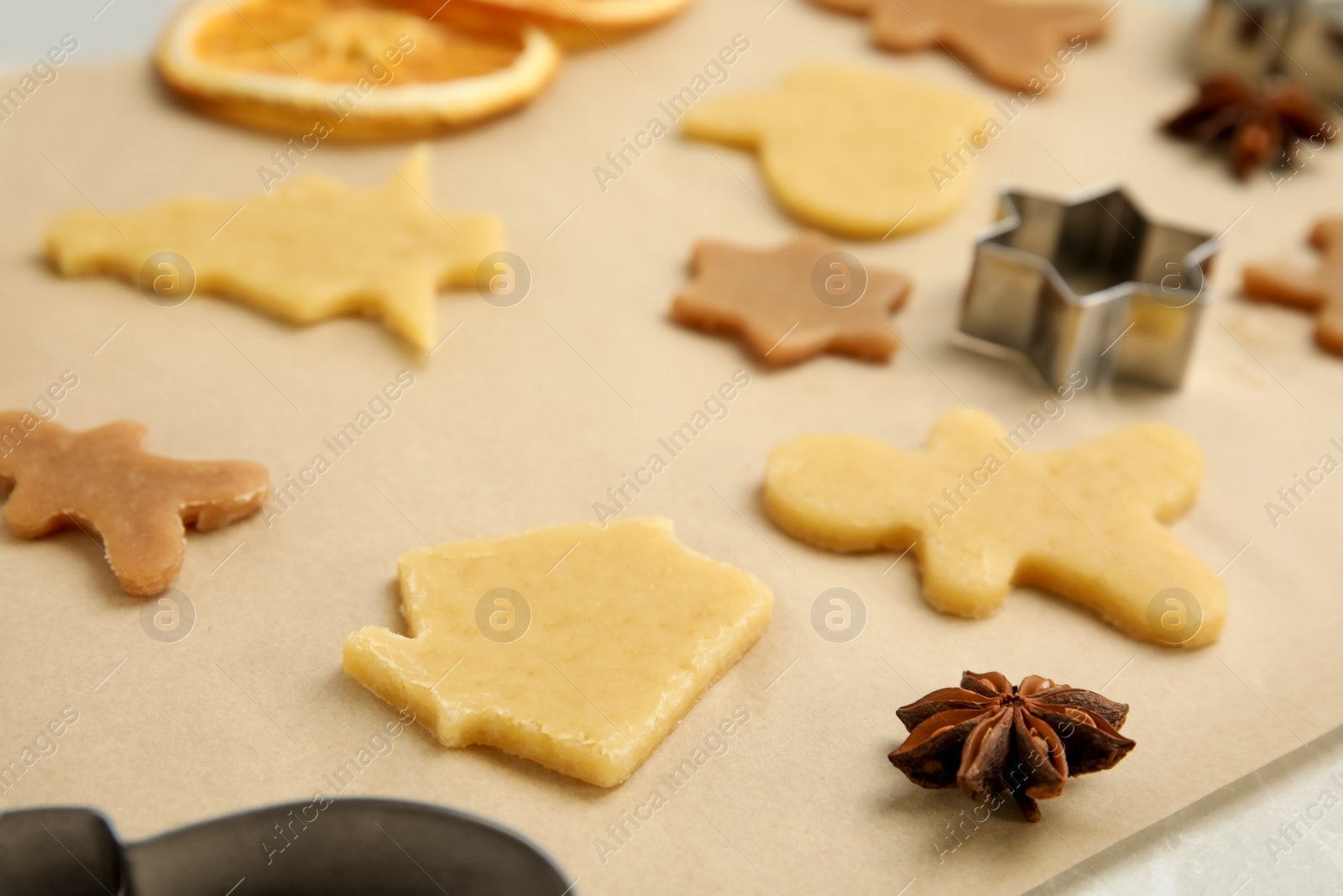 Photo of Unbaked cookies and cutters on parchment paper, closeup. Christmas biscuits