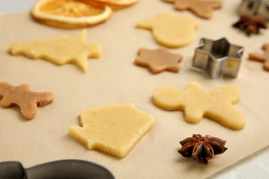 Photo of Unbaked cookies and cutters on parchment paper, closeup. Christmas biscuits