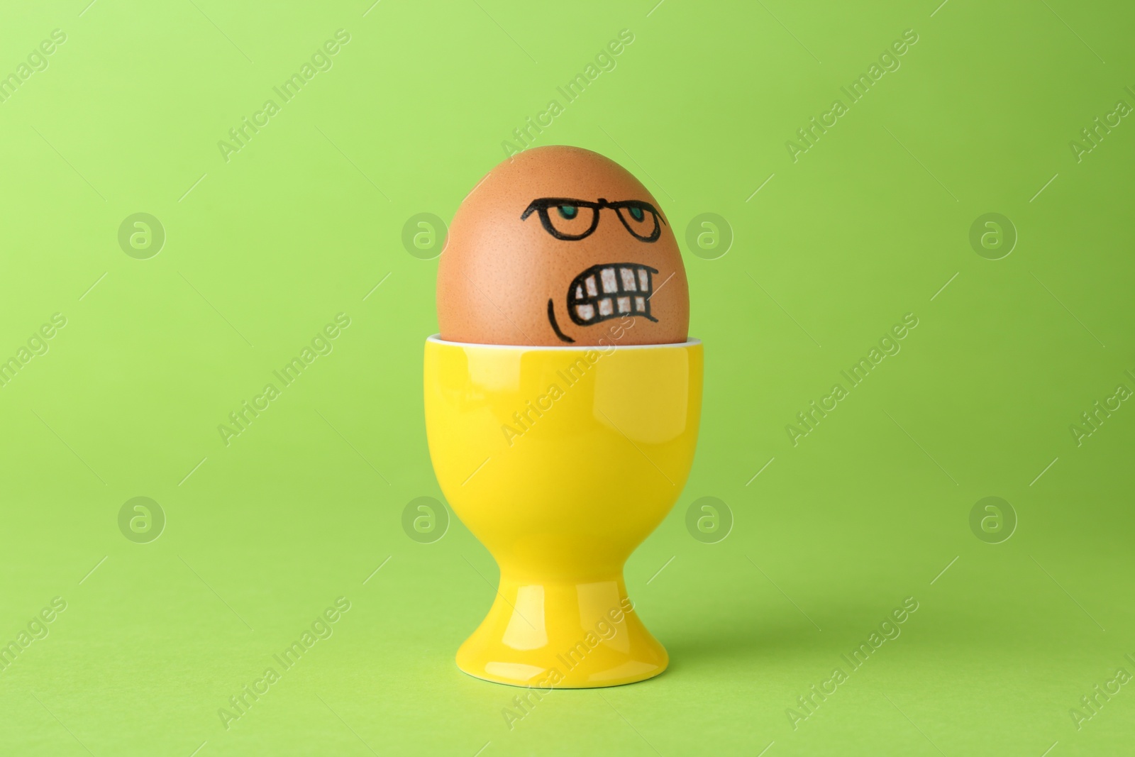 Photo of Egg with drawn angry face in cup on green background