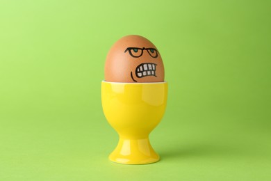 Photo of Egg with drawn angry face in cup on green background
