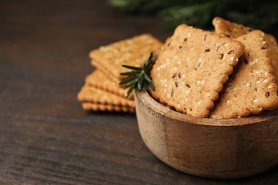 Photo of Cereal crackers with flax, sesame seeds and rosemary in bowl on wooden table, closeup. Space for text