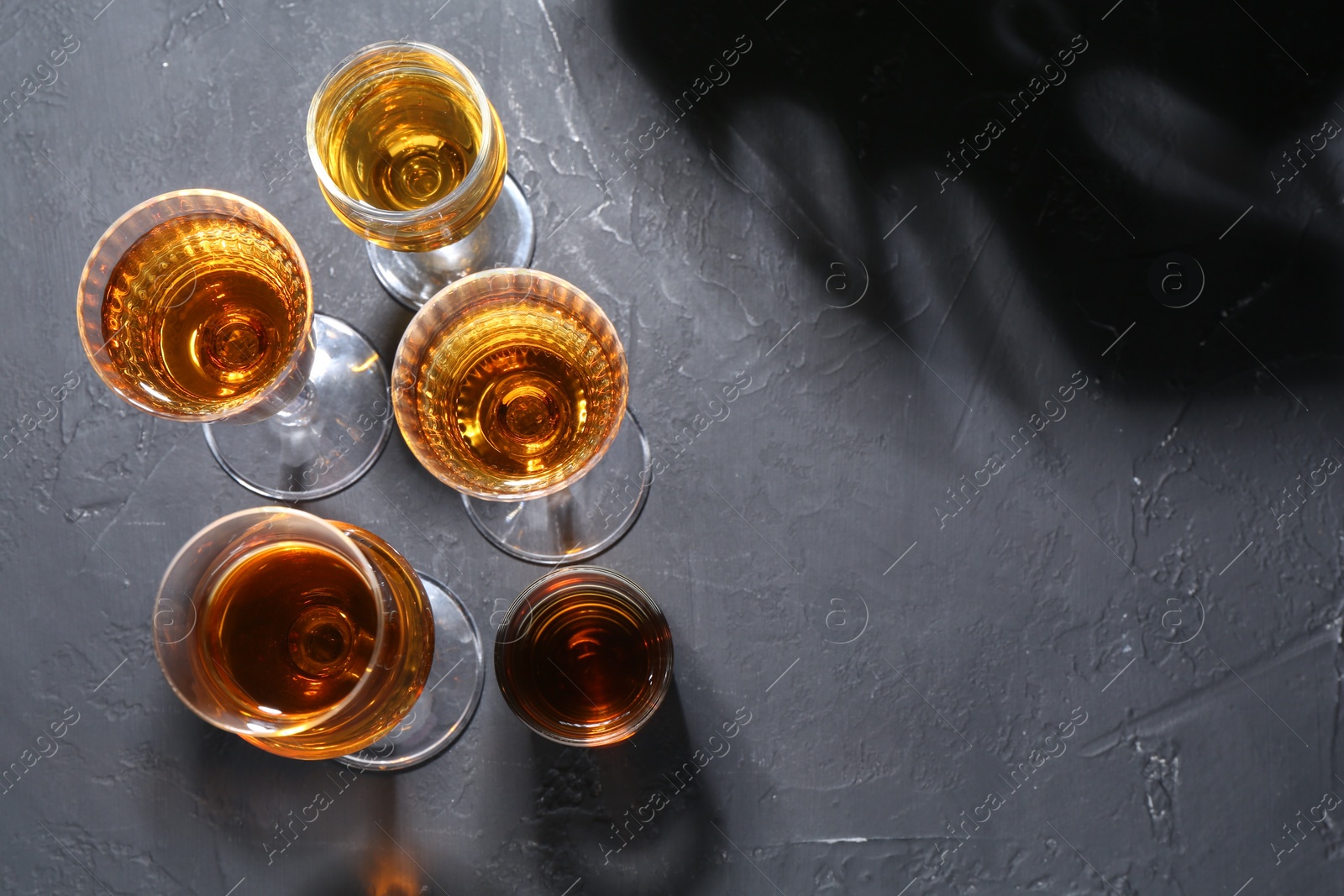 Photo of Many different liqueurs in glasses on dark textured table, flat lay. Space for text