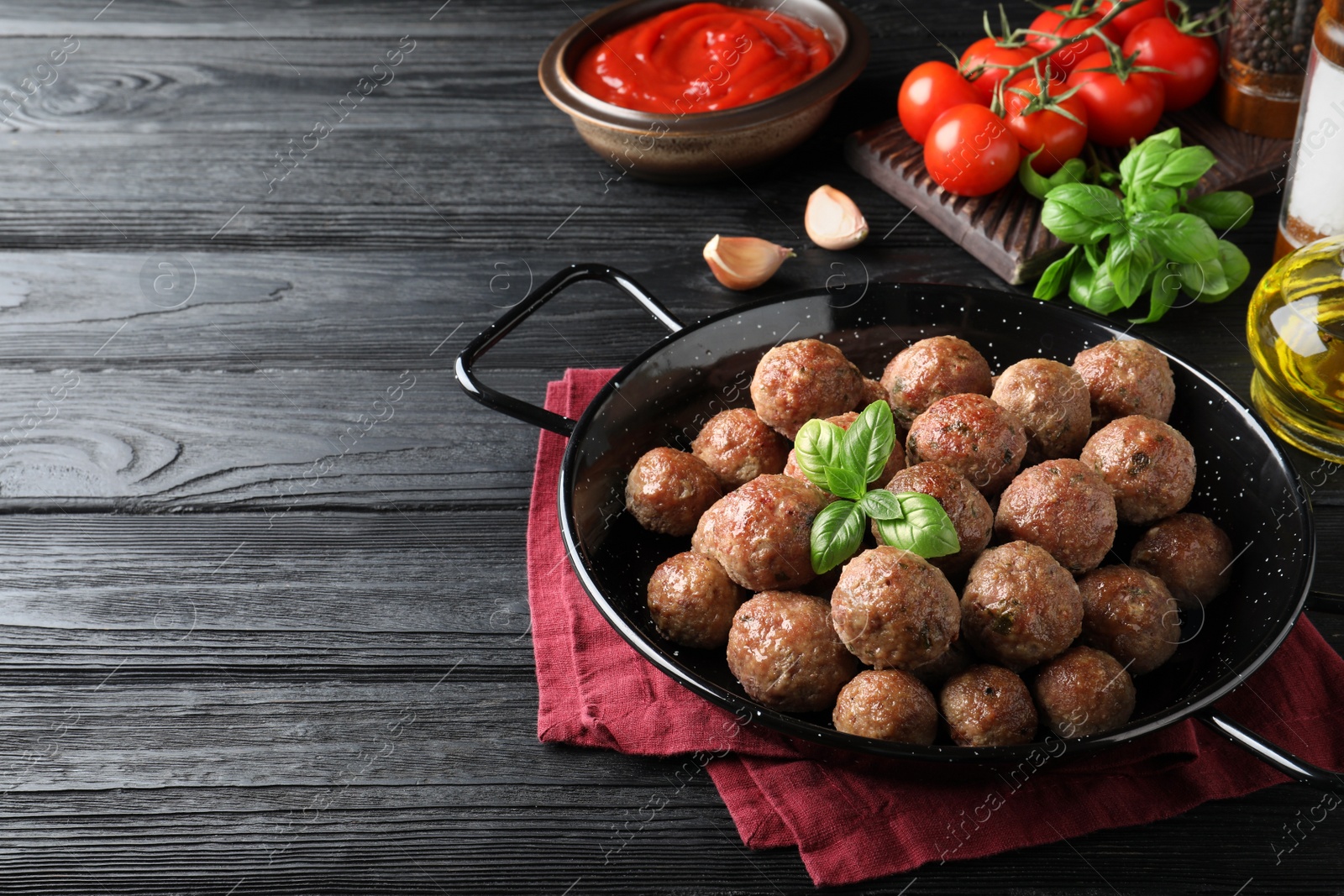 Photo of Tasty cooked meatballs with basil on black wooden table. Space for text