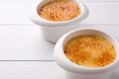 Photo of Delicious creme brulee in bowls on white wooden table, closeup