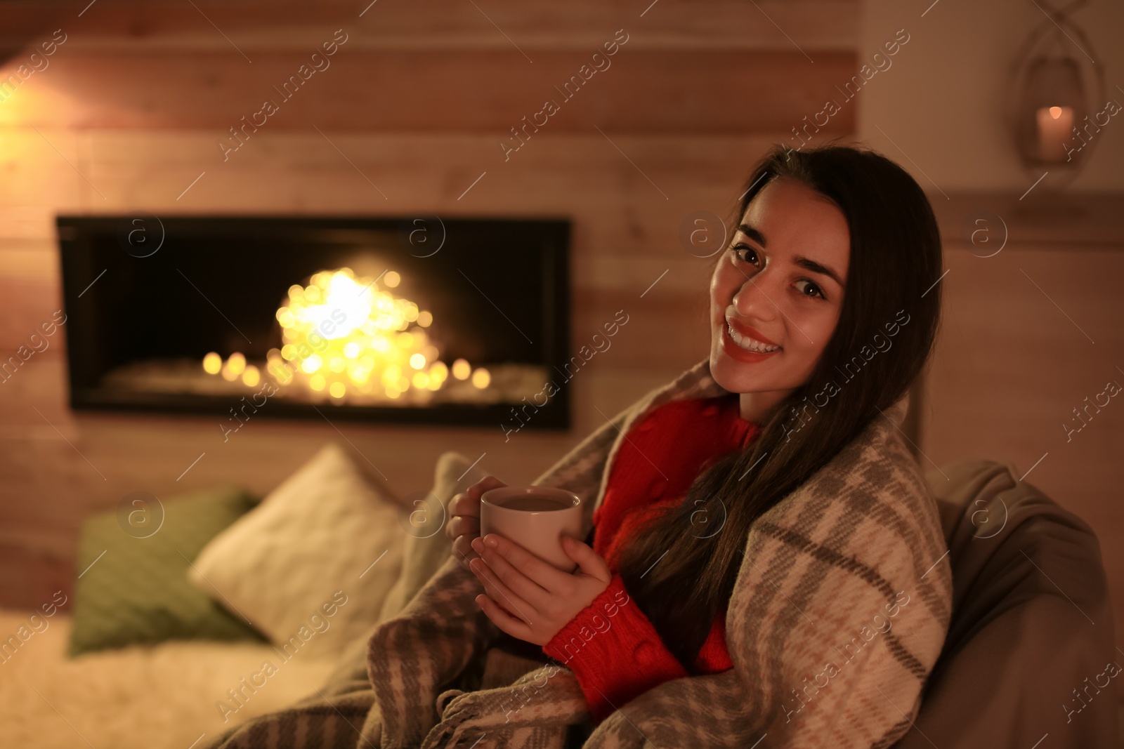 Photo of Young woman drinking coffee near decorative fireplace at home. Winter season