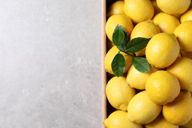 Photo of Fresh lemons in wooden crate on grey table, top view. Space for text