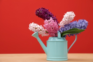 Photo of Beautiful hyacinths in watering can on table against color background, space for text. Spring flowers