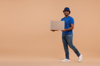 Photo of Happy young courier with parcel on light brown background, space for text