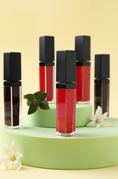 Photo of Different lip glosses, podiums and flowers on beige background