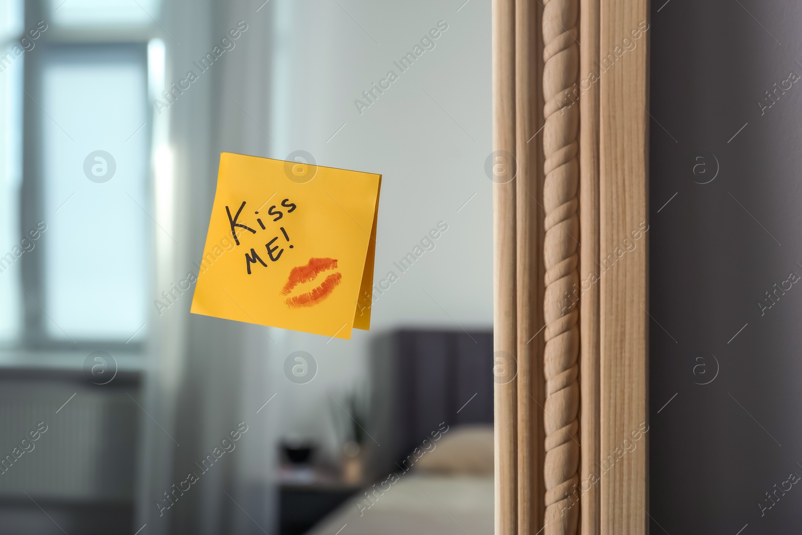 Photo of Sticky note with phrase Kiss Me and lipstick mark attached to mirror in room