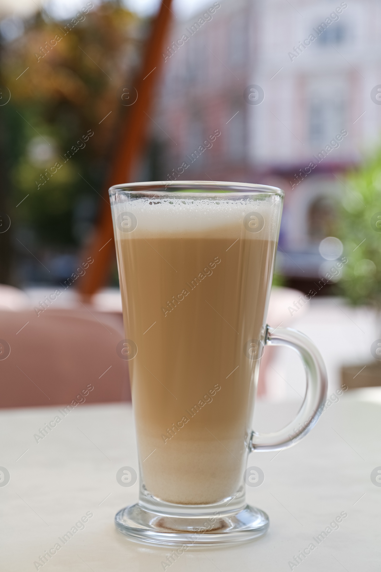 Photo of Glass with delicious coffee on white table in outdoor cafe