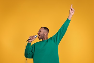 Photo of Handsome man with microphone singing on orange background