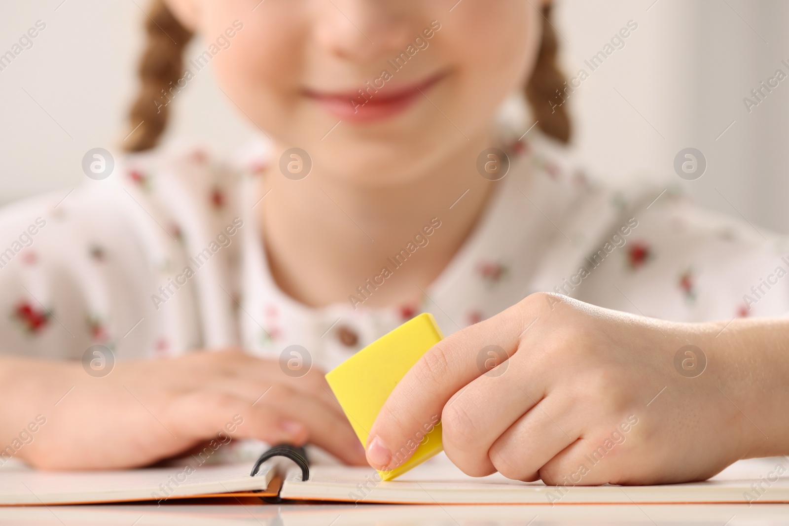 Photo of Girl using eraser at white desk, closeup