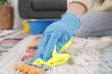 Photo of Woman in rubber gloves cleaning carpet with rag indoors, closeup