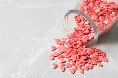 Photo of Pink heart shaped sprinkles and overturned glass jar on light grey table. Space for text