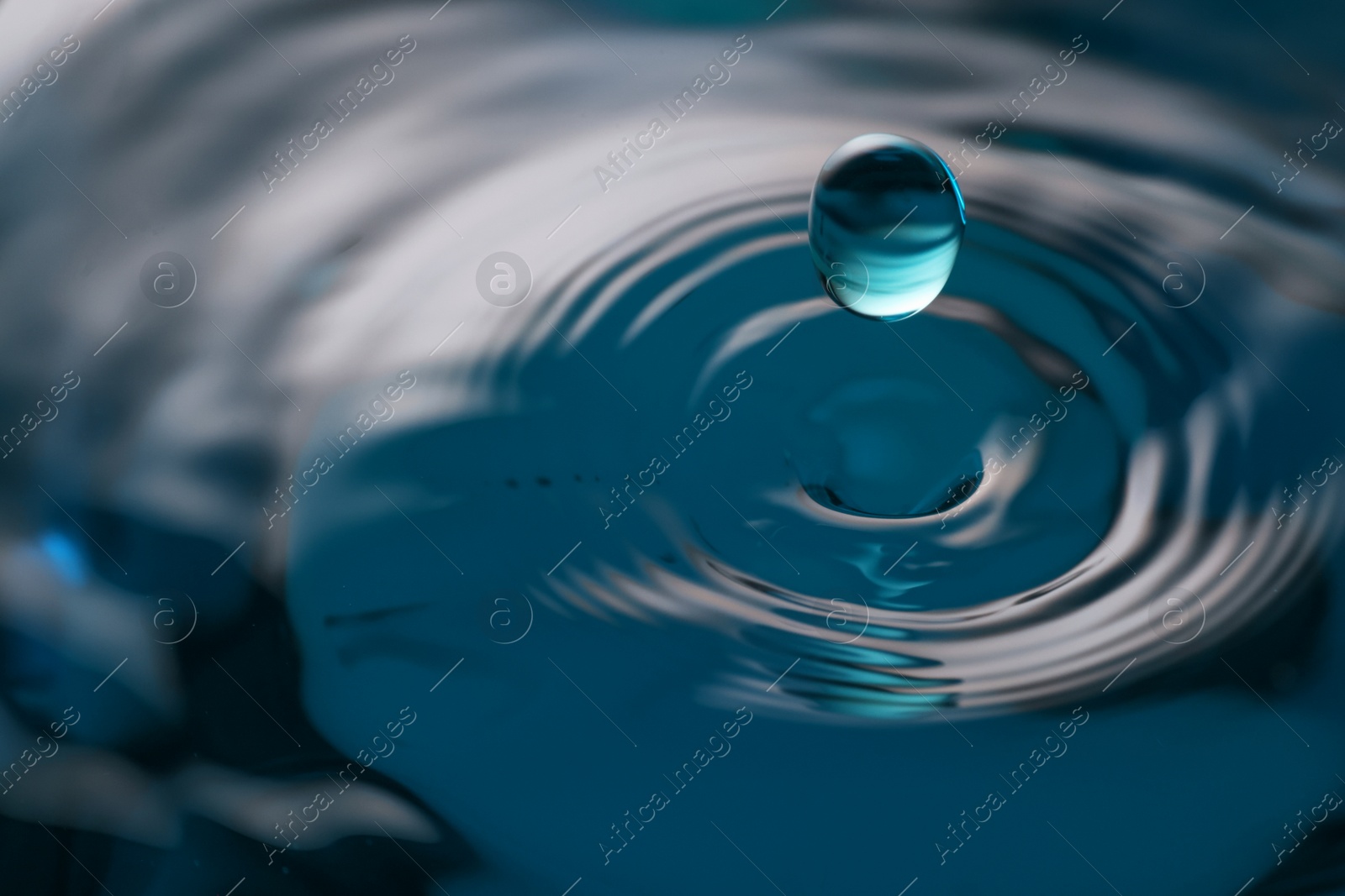 Photo of Drop falling into clear water on blue background, closeup