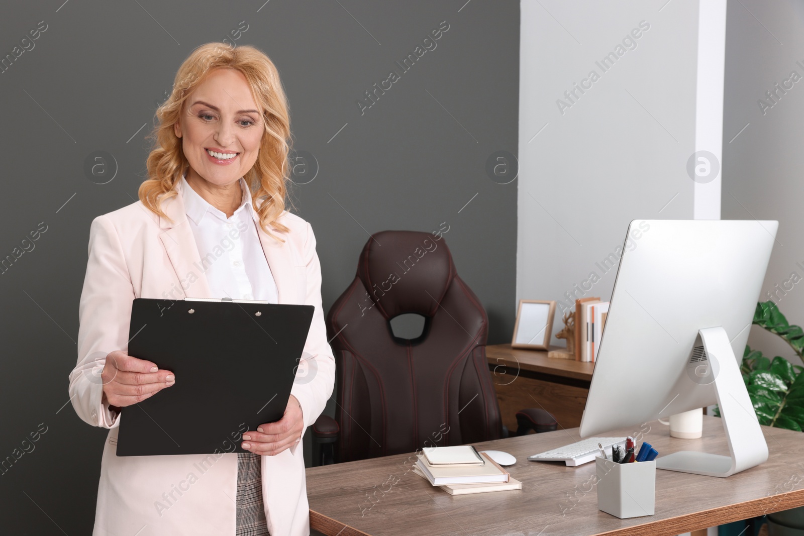 Photo of Happy lady boss with clipboard near desk in office. Successful businesswoman
