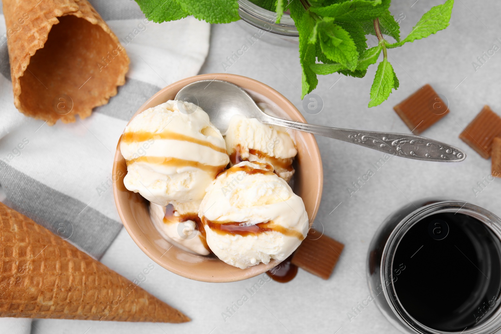 Photo of Scoops of ice cream with caramel sauce, wafer cones and candies on light grey table, flat lay