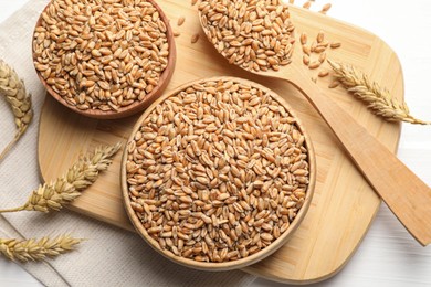 Photo of Wheat grains in bowls and spoon on wooden board, flat lay