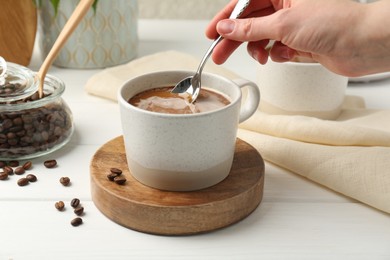 Photo of Woman stirring coffee with spoon at white wooden table, closeup