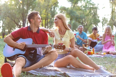 Young man playing guitar for his girlfriend in park. Summer picnic