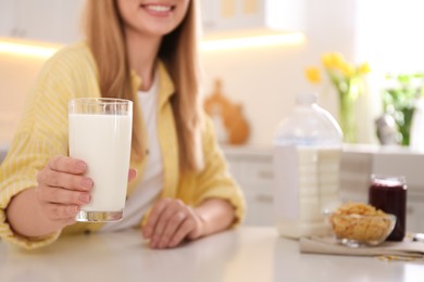 Photo of Young woman with gallon bottle of milk, glass and breakfast cereal at white table in kitchen, closeup