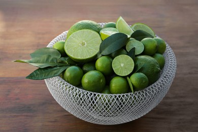 Photo of Fresh ripe limes and green leaves in bowl on wooden table
