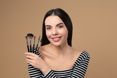 Photo of Happy woman with different makeup brushes on light brown background