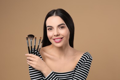 Happy woman with different makeup brushes on light brown background