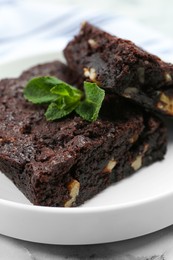 Delicious brownies with nuts and mint on plate, closeup
