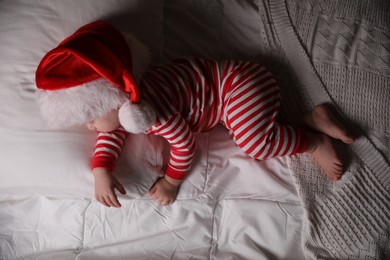 Baby in Christmas pajamas and Santa hat sleeping on bed, top view