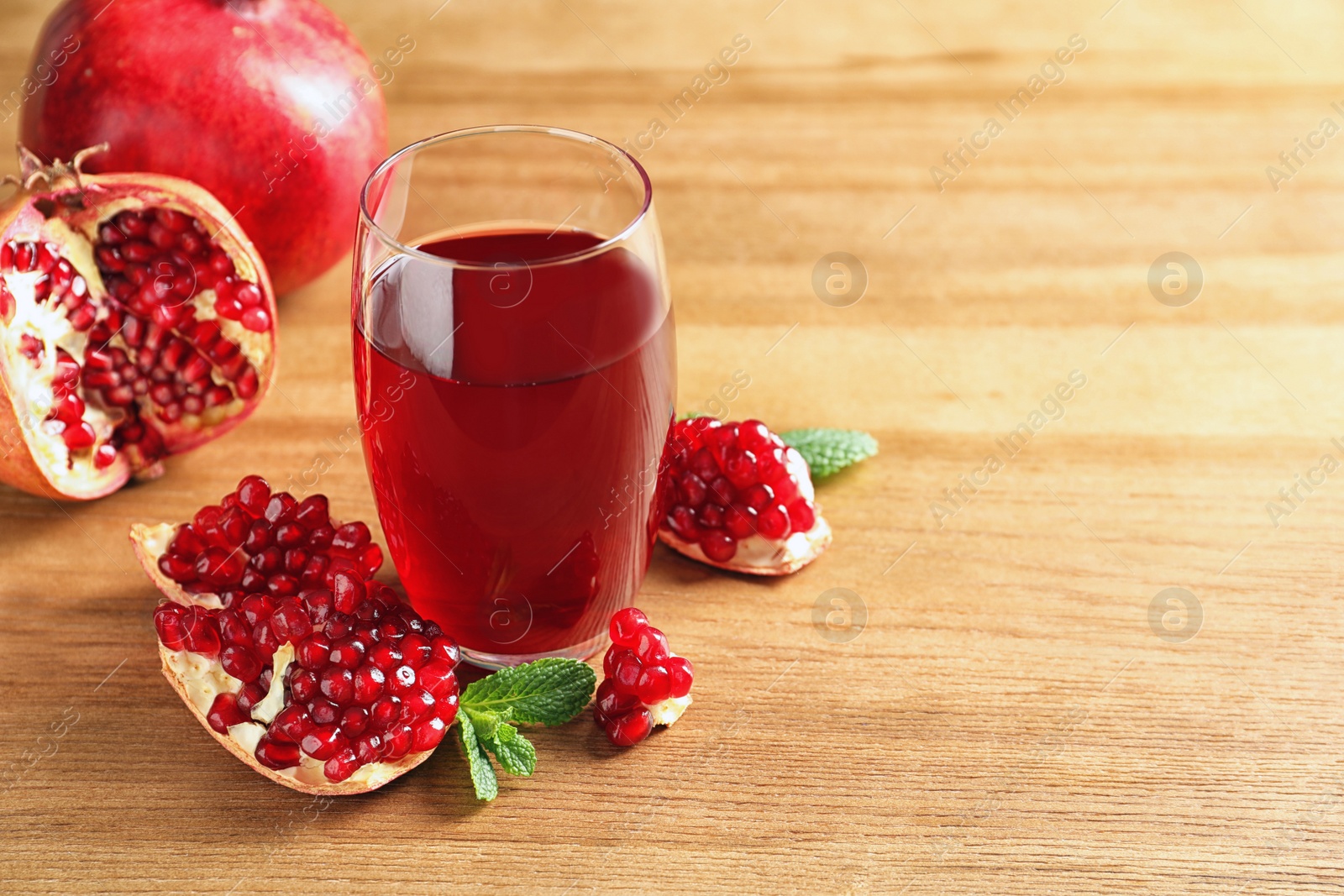 Photo of Glass of pomegranate juice and fresh fruits on wooden background, space for text