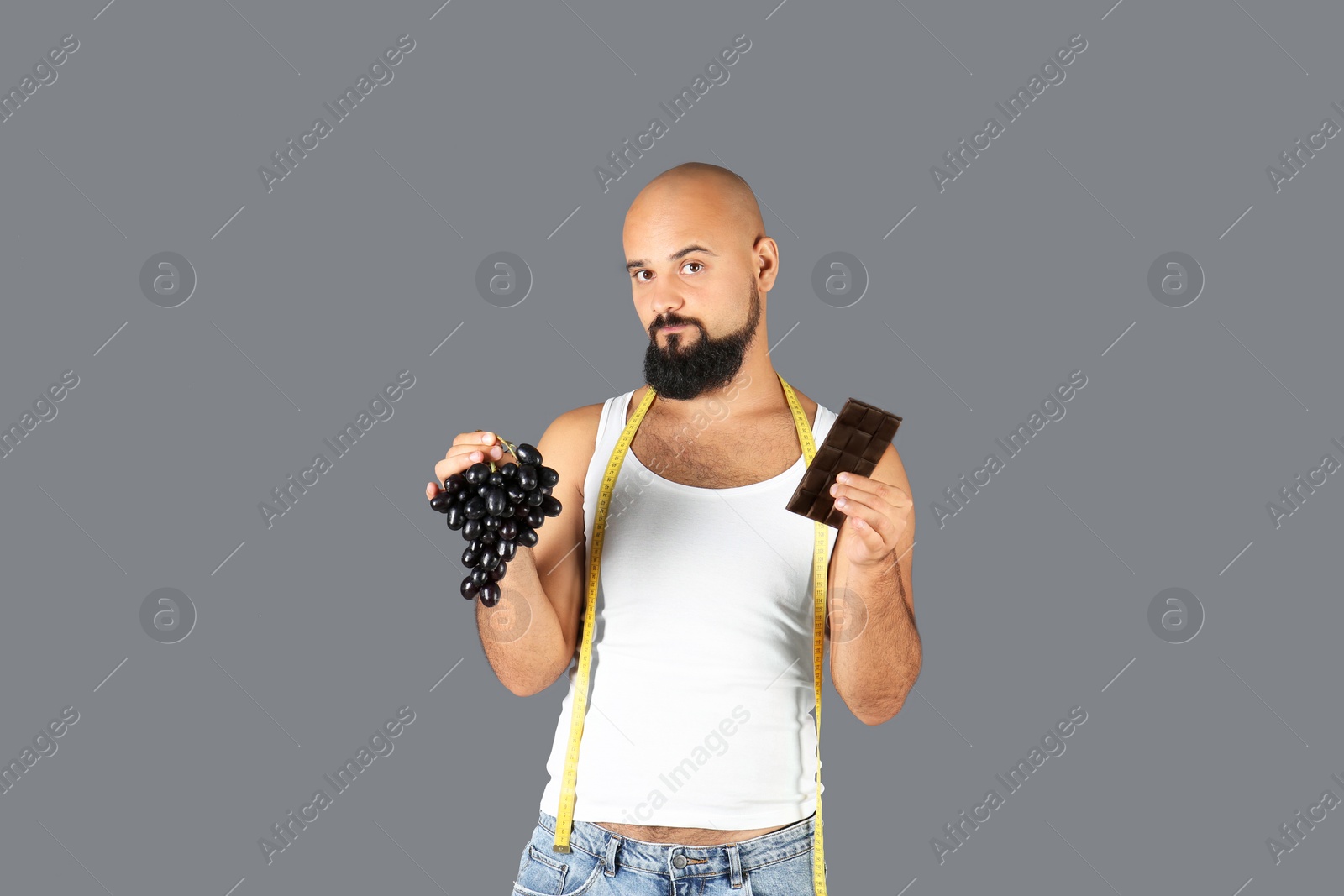 Photo of Overweight man with grapes, chocolate bar and measuring tape on gray background